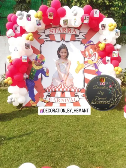 A close-up of the personalized carnival theme backdrop. It features a large photo of the birthday girl, fun clown illustrations, and is framed with red and white balloons, with small photos clipped on for a personal touch.