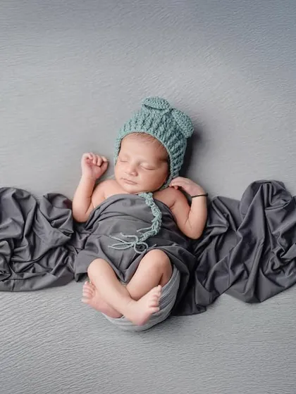 The classic "potato sack" pose, where the baby is snugly wrapped to feel secure and sleepy. The simple grey tones and flowing fabric create a timeless and elegant newborn portrait.