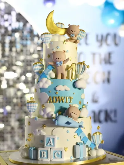 An incredible three-tiered cake for the "Love You to the Moon & Back" party. The cake is adorned with teddy bears, clouds, stars, and a crescent moon, perfectly matching the theme.