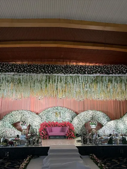 A beautiful stage with three large, curved floral structures made of white flowers, creating a soft and elegant backdrop.