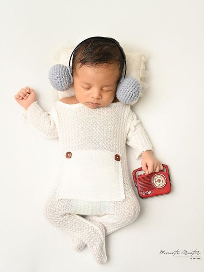 Lost in the music. This newborn, dressed in a simple white outfit, sleeps with tiny headphones and a miniature radio.