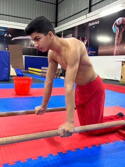 A young student practices a dip on the parallettes. This is a foundational calisthenics exercise for building chest, shoulder, and tricep strength.