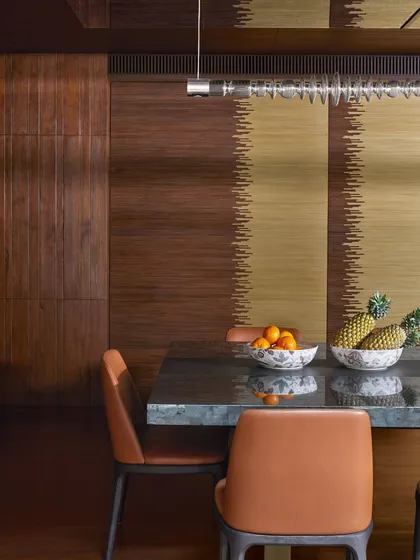 A detail of the Baid Residence dining table, showing the contrast between the cool stone top and the warm leather chairs. A custom fluted brass and wood door is visible in the background.